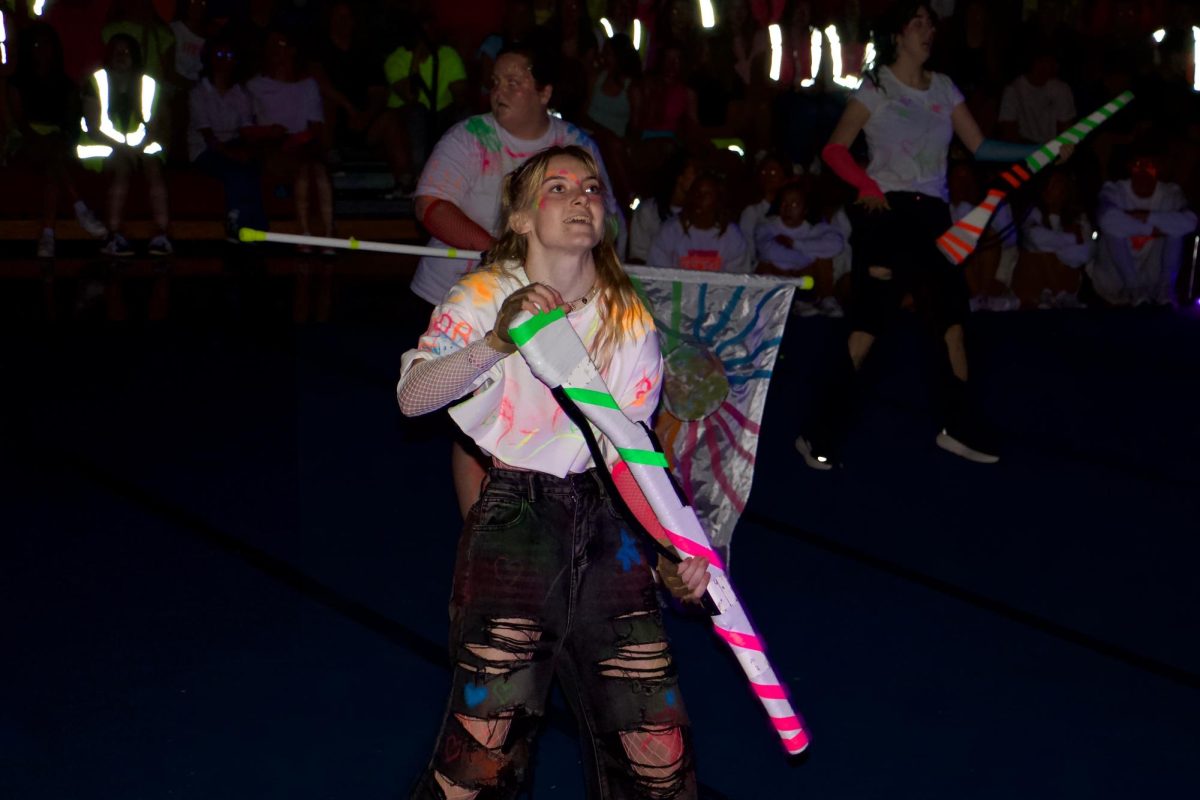 Mali Ayers, a senior color guard member, prepares to throw a neon rifle into the air. 