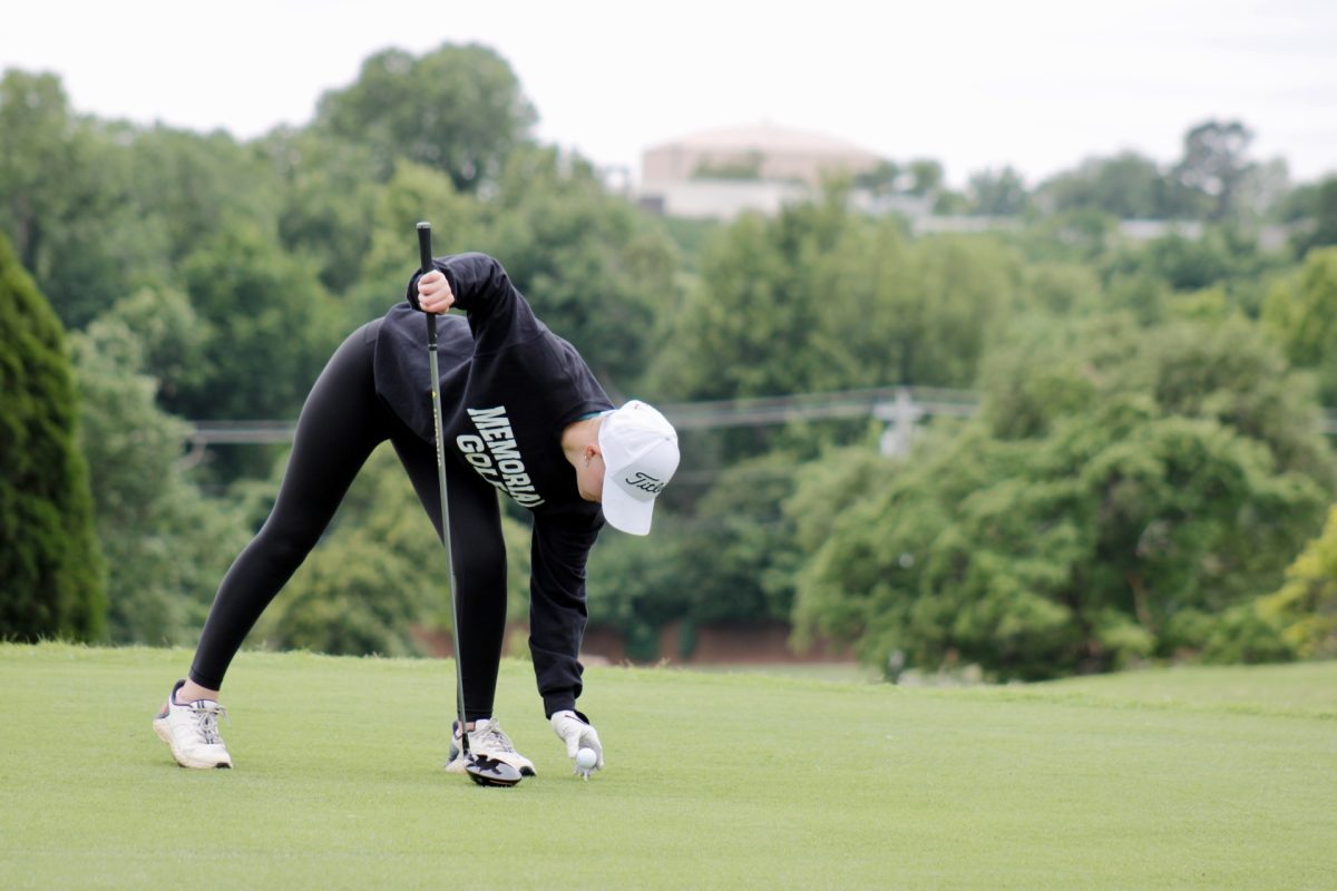 Junior Stella Colby places the golf ball on the tee shot on the turf before striking it.
